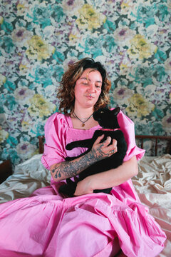 Woman with pink dress holding black cat in bedroom