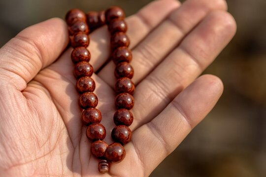 Close-up of a hand holding a brown wooden bead necklace
