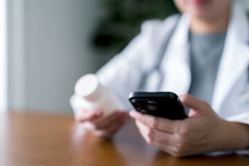 Close-up of doctor checking pill bottle and using smartphone. Online healthcare, telemedicine, digital prescriptions, virtual consultations and remote medical services in modern medicine.