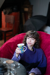 young beautiful woman drinking tea in armchair in studio