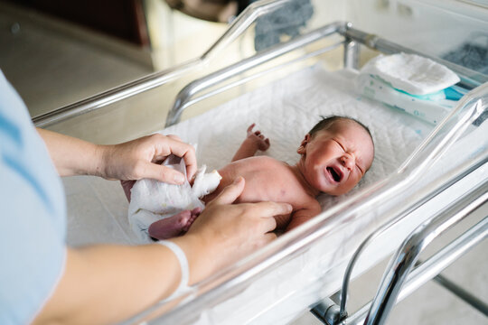 Nurse cleaning newborn baby after cesarean section in hospital crib