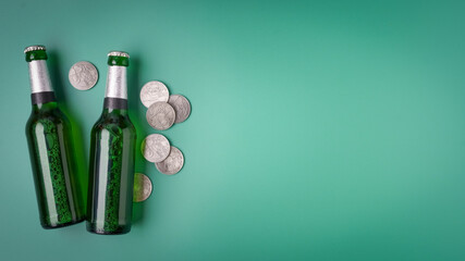 St. Patrick's Day concept green beer bottles and coins on green background with copy space, top view