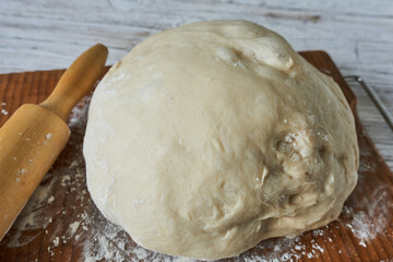 Raw dough on a cutting board with a rolling pin. Close-up.