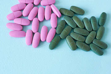 Pink and green pills on blue background. Focus on foreground, soft bokeh.
