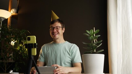 Enthusiastic influencer wearing colorful party hat unboxing birthday gifts while recording video blog, engaging social media followers with genuine excitement and joy
