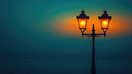 Illuminated double lamp post at dusk by the sea, emitting warm light against a dark teal sky.