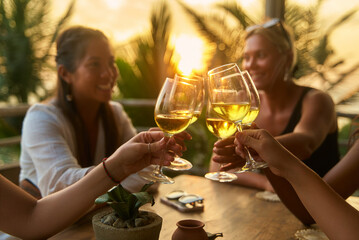 Diverse women at restaurant toasting with wine. Friends enjoy dinner party with smiles and relaxation. Evening social event in vibrant setting. Celebration with laughter and connection.