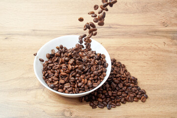 Coffee beans in a cup and on the table and falling from above.