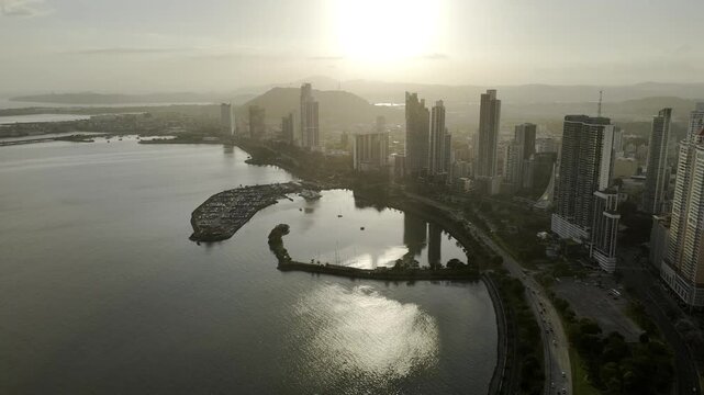 Drone flies into sunset with Cinta Coster and Panama Yacht and Fishing Club in silhouette n Panama City