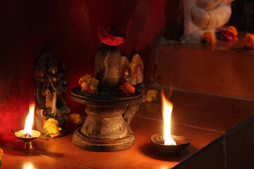 a tiny shiva-linga with flowers on it, in between lamp lights 
