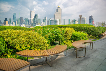 Fototapeta premium Bangkok Iconsiam park. Green flower bed with wooden bench and many modern tall buildings and skyscrapers at a viewing point of the largest shopping mall in the city