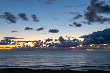 Cloudscape at sunset over the sea with dark clouds in front of a sky changing from blue to orange