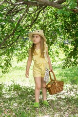 Obraz premium Serious little girl in a yellow dress and straw hat carrying a heavy basket lost in the woods.
