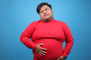 Hungry Young Fat Guy Touching His Belly Isolated on Blue Background