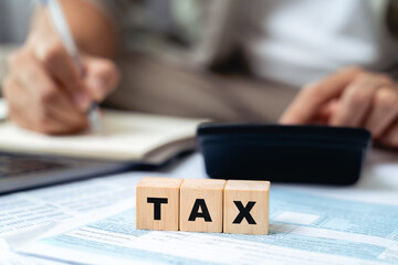 Man is calculating annual tax with calculator with TAX text on wooden block