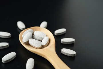 white Pills Medicine tablet capsules in a wooden spoon blister pack on a black background