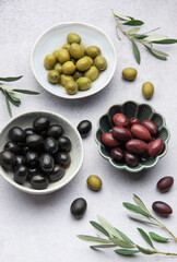 Black, green and kalamata olives with olive branches in bowls on marble