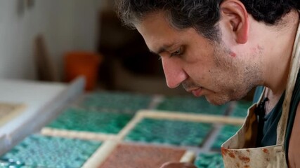 Artisan focusing intently on creating intricate mosaic designs, demonstrating craftsmanship and attention to detail in an artistic workspace
