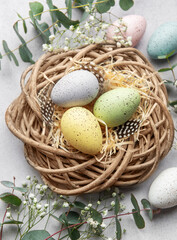 Fototapeta premium Easter eggs lying in nest surrounded by flowers and eucalyptus leaves