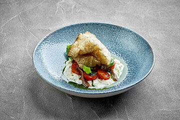 A vibrant and appetizing plate of burrata cheese topped with cherry tomatoes, anchovies, and fresh herbs.