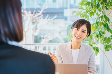 明るい窓際で対面する人物に質問をする30代の転職のアドバイザーの女性