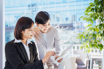 ビジネス街にある明るいオフィスで協力して仕事を進めるチームワークの良い2人の女性