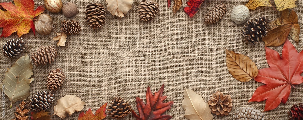 Aufkleber Autumn leaves and pine cones creating a frame on a burlap background with copy space in the center