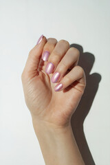 A close-up of a hand with pearl pink nails against a clean white background