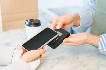 飲食店でテイクアウトコーヒーをスマートフォンのタッチ決済で購入する女性の手元