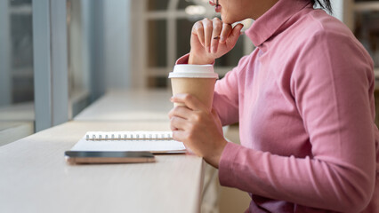A woman contemplating about work, as she reads and sips her coffee while sitting in a coffee shop.