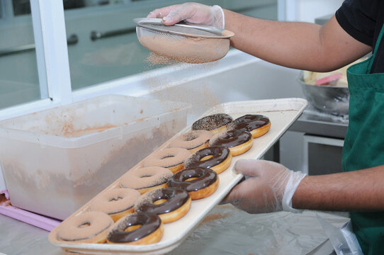 baker using strainer dusting cocoa powder into donut with chocolate glazing