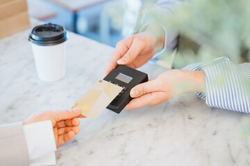 テイクアウトのコーヒーの購入と支払いをICチップの決済で行う女性の手元