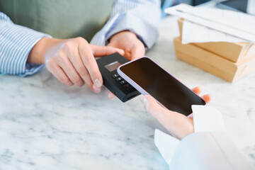 店舗で買う商品の支払いをスマートフォンのタッチ決済で行う女性の手元