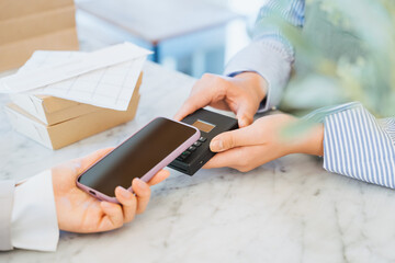 店舗で購入したテイクアウトの食事の支払いをスマートフォンのタッチで決済する女性の手元