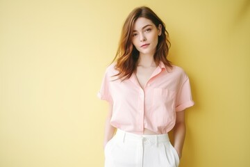 Obraz premium A woman in a pink shirt and white pants is standing in front of a yellow wall