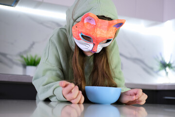 Young girl in casual quad style clothes with cat style mask. Cute child wearing a mask at home in kitchen.
