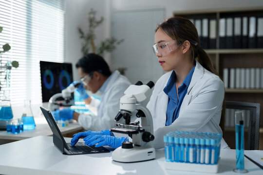Scientists working diligently in a laboratory setting, using microscopes and laptops. Test tubes and scientific equipment surround them, highlighting a focus on research and innovation