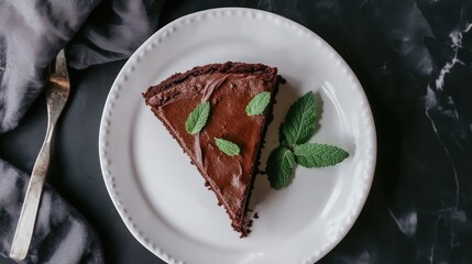 A decadent chocolate cake garnished with fresh mint leaves, elegantly placed on a white porcelain plate