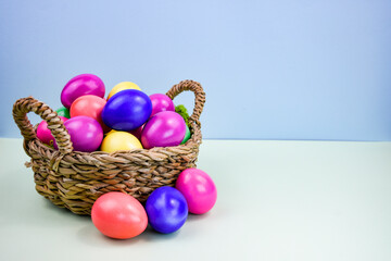 Easter composition with a basket filled with bright multi-colored eggs on a light background.