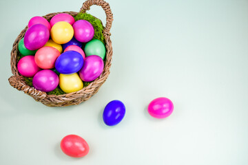 Easter composition with a basket filled with bright multi-colored eggs on a light background.