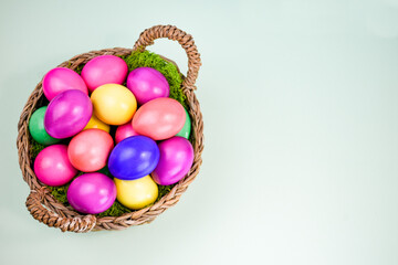 Easter composition with a basket filled with bright multi-colored eggs on a light background.