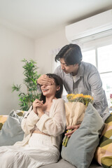 Asian young man surprises his beautiful girlfriend with flowers at home. 
