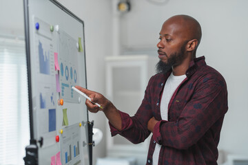 Business professional analyzing charts and graphs on a whiteboard, focused on data-driven...