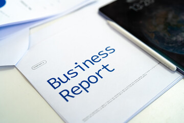 A business report document sits on a desk next to a tablet and pen, emphasizing professional work and analysis.