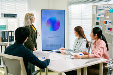 A business meeting with four professionals discussing data displayed on a screen, showcasing...