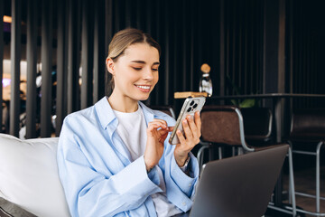 Smiling businesswoman using smartphone and working on laptop in modern office
