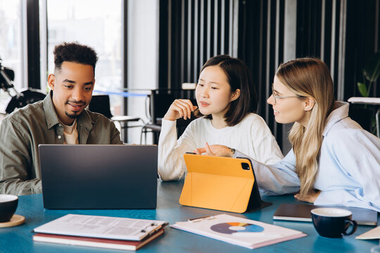 Diverse business team collaborating on project using laptop and tablet in modern office