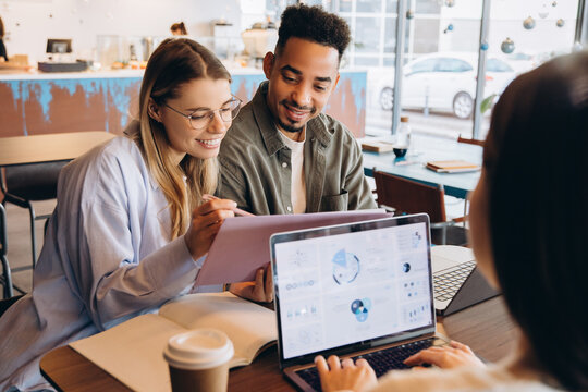 Businesspeople working on charts and graphs in cafe meeting using laptop and documents