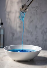 Whisk lying flat against the edge of a white ceramic bowl filled with a clear blue liquid, wire whisk, calm color