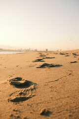 Close-up of footprints in the sand at a serene beach during sunset, with a distant city skyline